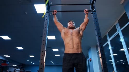 Shirtless man pulling up on horizontal bar. Crossfit athlete doing abs exercises on horizontal bar