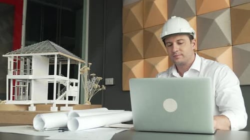 Architect Using Laptop with Model House and Blueprints