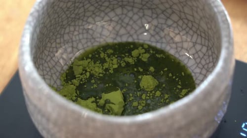 Extreme close up shot of hot water added into ceramic cup with matcha powder, preparation of ceremon