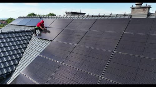 Worker Installing Solar Panels on House Rooftop