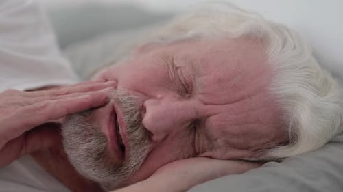 Close up of Old Man with Toothache Lying on Side in Bed