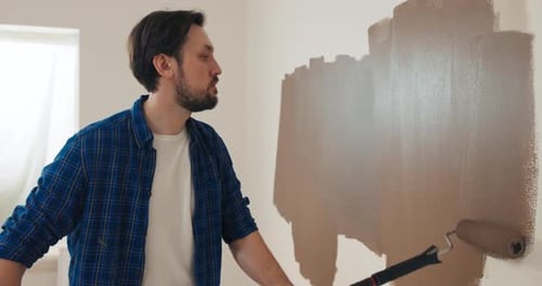 Mann mit dunklem Haar und Bart hält Roller in den Händen und konzentriert sich auf das Bemalen von Wänden im Leben