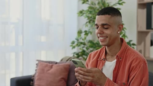 Close View of the Happy Multi Ethnic Man Sitting on the Sofa and Using Smartphone