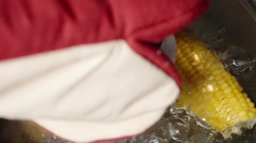 Two boiled corn cobs are simmering in a pot as I lift the lid. The camera moves in a dolly motion.