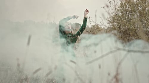 Model posing with arms raised in smoke filled meadow