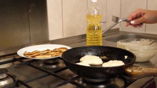 13 1Pfannkuchen werden in einer Pfanne gebraten, einige goldbraun und eine noch roh. Eine Hand dreht eine Krawatte mit