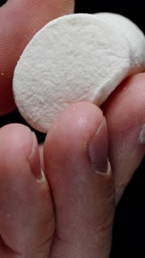 Vertical video. Round Marshmallow Squeezed in Hand Against a Black Background. Soft Sugar Texture.
