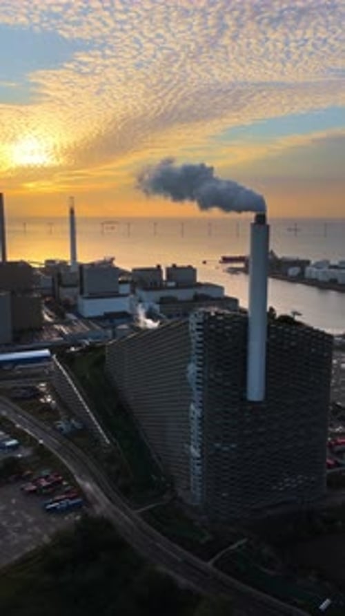 Aerial drone view of CopenHill energy plant with smoking chimneys, overlooking the sea and offshore