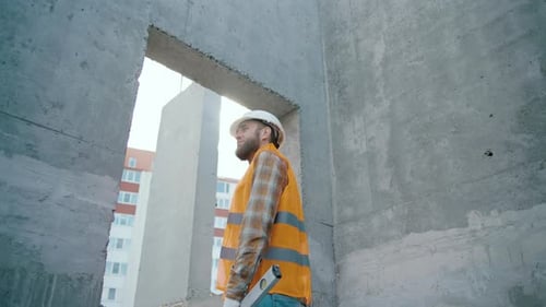 Back view of tired builder looking out of window at construction site. Mature construction worker