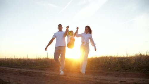 Wife and Husband Lift Daughter Walking Against Setting Sun