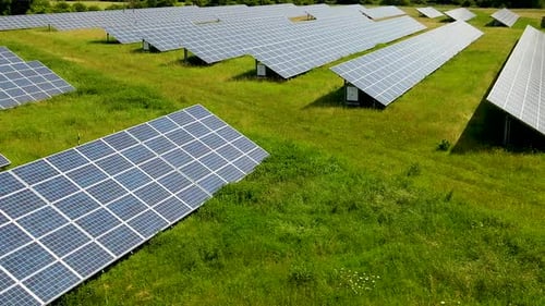 Aerial fly over array of solar panels installed in a green field