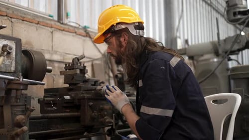 Blue collar worker is working at machine shop with welding robot arm.