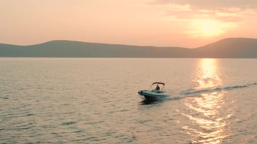 Aerial view of a woman driving speed boat towards the camera. Beautiful sunset sea view.