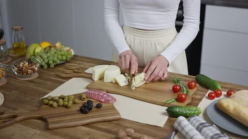 Gros plan de mains féminines dans le cadre Une femme au foyer dans la cuisine coupe des tranches de fromage et prépare
