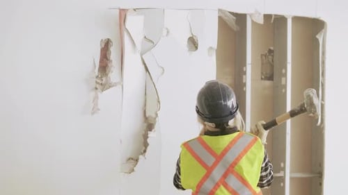 Woman demolishing partition wall in slow motion during office redevelopment project