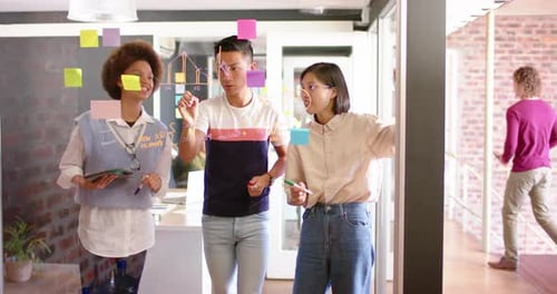 Três colegas criativos diversos, homens e mulheres, discutindo ideias em uma parede de vidro, em câmera lenta