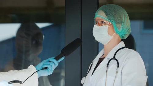 Un médecin donne une interview à un journaliste, tous deux en tenue de protection
