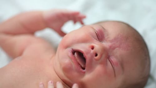 Close up of a newborn baby girl crying lying on a pink blanket in her bed