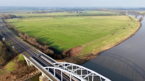 Aerial view of arched highway bridge over curving river, linking green fields, trees, and scattered
