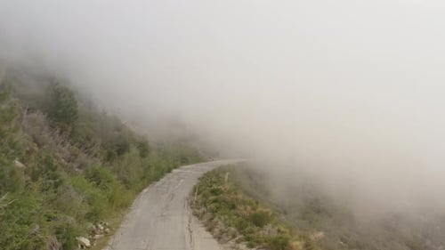 Drone view of windy road on side of mountain vanishing into clouds. Aerial view of a mountain road i