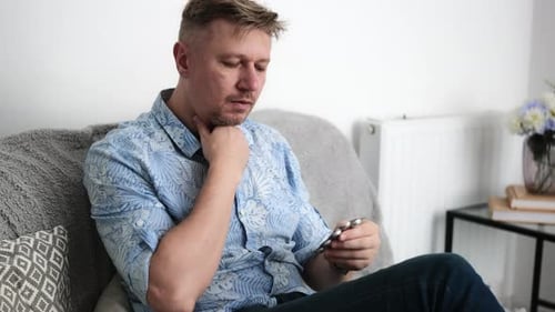 Man Holds Medicine Blister Pack and Touches Throat