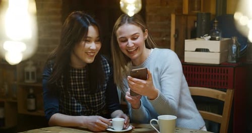 Slow motion of beautiful young girls having coffee at cafe and having fun with mobile cell phone.