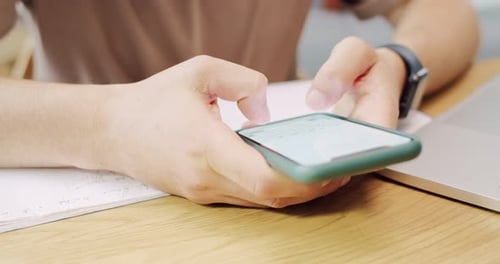 Nahaufnahme eines Mannes, der am Schreibtisch sitzt, sein Smartphone hält und drinnen chattet, männliche Hände mit Handy
