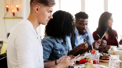 Friends Eating Together at Restaurant Looking at Phone