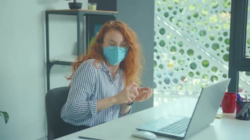 Young Woman Employee in a Medical Facial Mask Works in the Office Use Antiseptic Laptop Coronavirus