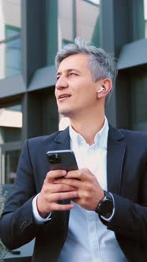 Businessman Using Smartphone Outdoors Standing on City Street Smiling Looking to Mobile Phone Screen