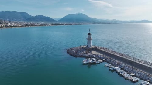 Aerial Video of a Coastal White Lighthouse With a Flag Standing Tall in a Peaceful Bay With Bright