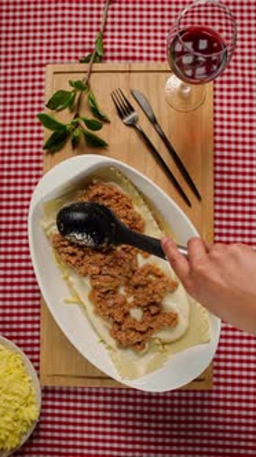 Woman Assembling Lasagna with Spoon on Red Plaid Table