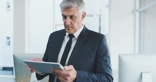 4k video footage of a handsome mature businessman using his tablet in the office