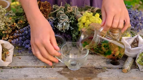 Hands Pouring Herbal Tea in a Rustic Setting
