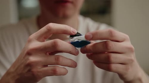 Gros plan recadré d'un homme tenant une capsule de détergent à lessive examinant des compartiments liquides colorés