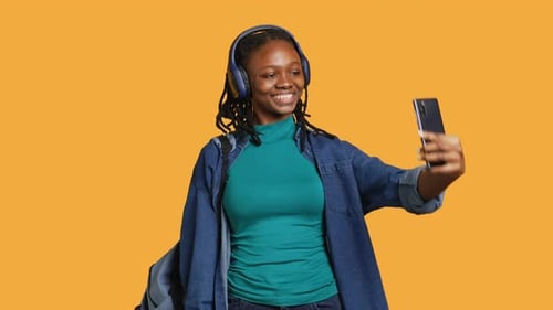 Cheerful Woman with Headphones Using Phone to Take Selfies Studio Background