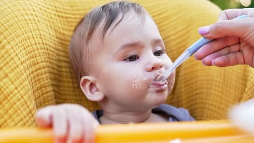 Baby nutrition from spoon. Cute Caucasian child with smudged face eating porridge. Close up
