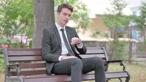Worried Man Checking Time on Bench in Park