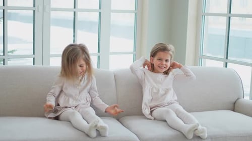 Two Adorable Girls Laughing on a Couch Indoors