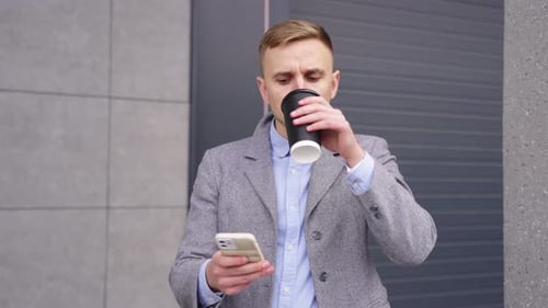 Man Checks Phone and Drinks Coffee Outside