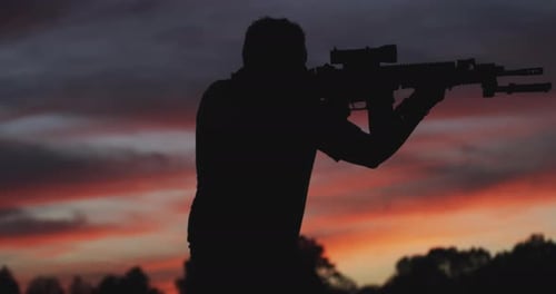 Silhouette Of Man Aiming With Assault Rifle At Sunset. medium shot, side view