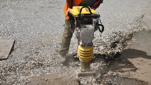 Ein Arbeiter verwendet bei Straßenreparaturen einen tragbaren Vibrationsstampfer