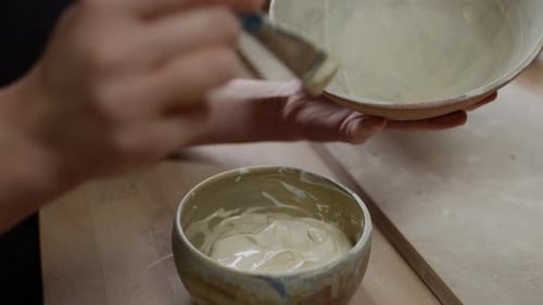 Person painting ceramic bowls in studio close up