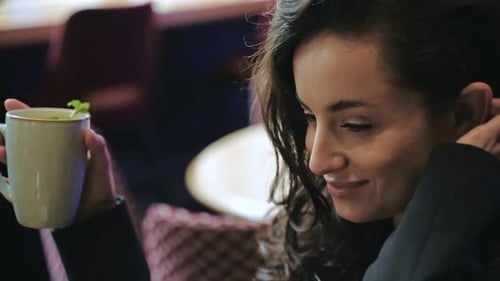 Caucasian Girl Sitting Inside of Cafe Drinking Hot Tea with Mint Touching Her Long Brown Hair