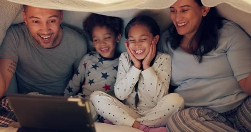 Family Laughing Together Under Blanket with Tablet