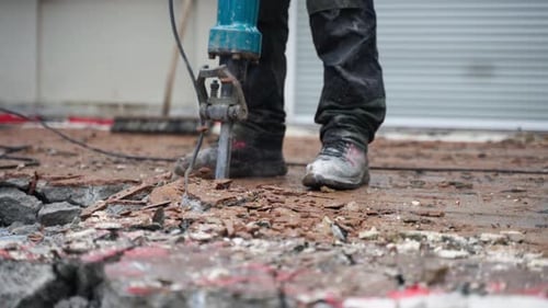 A construction worker using a jackhammer to remove old concrete near the house - close-up