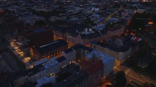 Backwards Fly Above Night City High Angle View of Streets and Buildings in Urban Borough Tilt Up