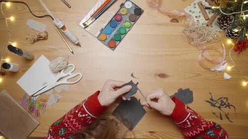 A Top-Down View of a Woman Crafting in a Red Sweater at a Table Filled with Art Supplies and Festive