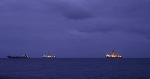 Several food processing boats moored in the distance at sea during the night illuminated by the ligh