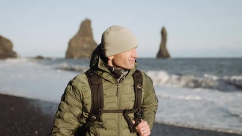 Man with backpack hiking along black beach